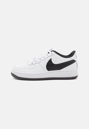 Baskets basses blanches avec le logo Nike noir, lacets blancs et bord de semelle noir, vues de profil sur un fond clair.