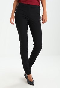 Pantaloni neri sartoriali dal taglio slim, con una trama di tessuto liscia e una cintura in vita, abbinati a décolleté nere a punta.