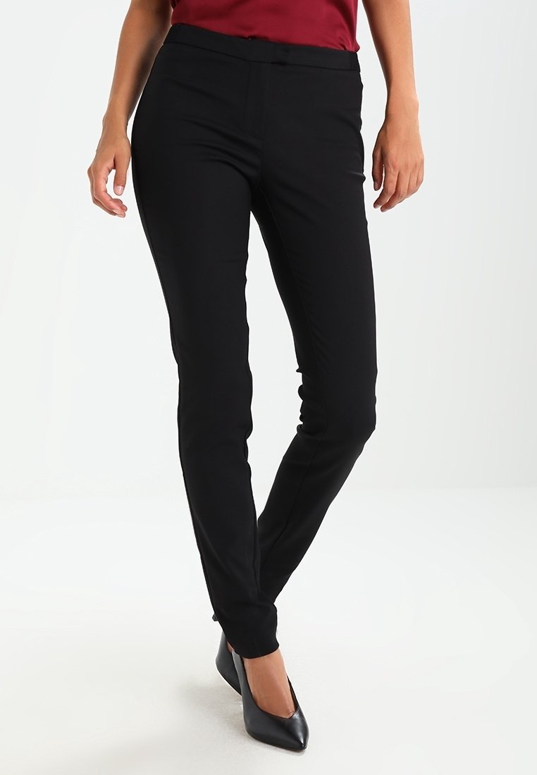 Pantaloni neri sartoriali dal taglio slim, con una trama di tessuto liscia e una cintura in vita, abbinati a décolleté nere a punta.