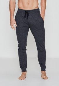 Graue Jogginghose mit Kordelzugbund, seitlichen Taschen, schmal zulaufenden Beinen und weicher Textur. Keine Muster oder sichtbaren Hardware-Elemente.