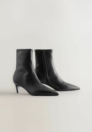 Bottes chevilles en cuir noir avec un bout pointu et une fermeture éclair. Caractérisées par un petit talon triangulaire et des détails de couture subtils.