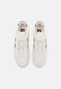 Hvite lær sneakers med burgunder detaljer, perforert tåboks, kremfargede lisser og en beige gummisåle. Logo vist på tungen.