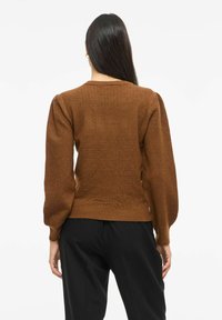 Brun teksturert genser med puffede ermer og ribbet kant. Designet har et subtilt mønster som skaper visuell interesse.