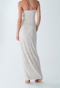 Abito da sera argento con paillettes, dalla silhouette aderente, spalline sottili e un design lungo e fluido. Dettagli superficiali texturizzati e scintillanti.