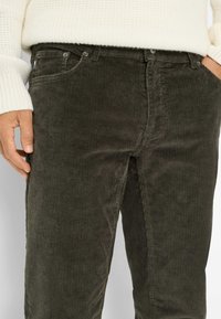 Donkergroene corduroy broek met verticale ribbeltextuur, vijf-pocketontwerp, metalen knoopsluitingen en een gladde afwerking.