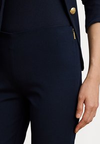 Ναυτικό μπλε εφαρμοστά παντελόνια από απαλό υλικό, που διαθέτουν κρυφό τσέπη με φερμουάρ και υφασμάτινη μέση. Χρυσά αξεσουάρ.