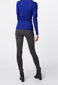 Maglione azzurro a maniche lunghe con texture a coste, abbinato a jeans skinny grigio scuro e stivaletti neri con tacco. Design semplice, silhouette aderente.