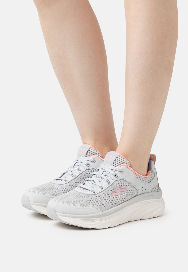 Ljusgrå sportskor med mesh-överdel, rosa detaljer och snörning. Tjock vit sula för dämpning och stöd. Märkbart logotyp på sidan.