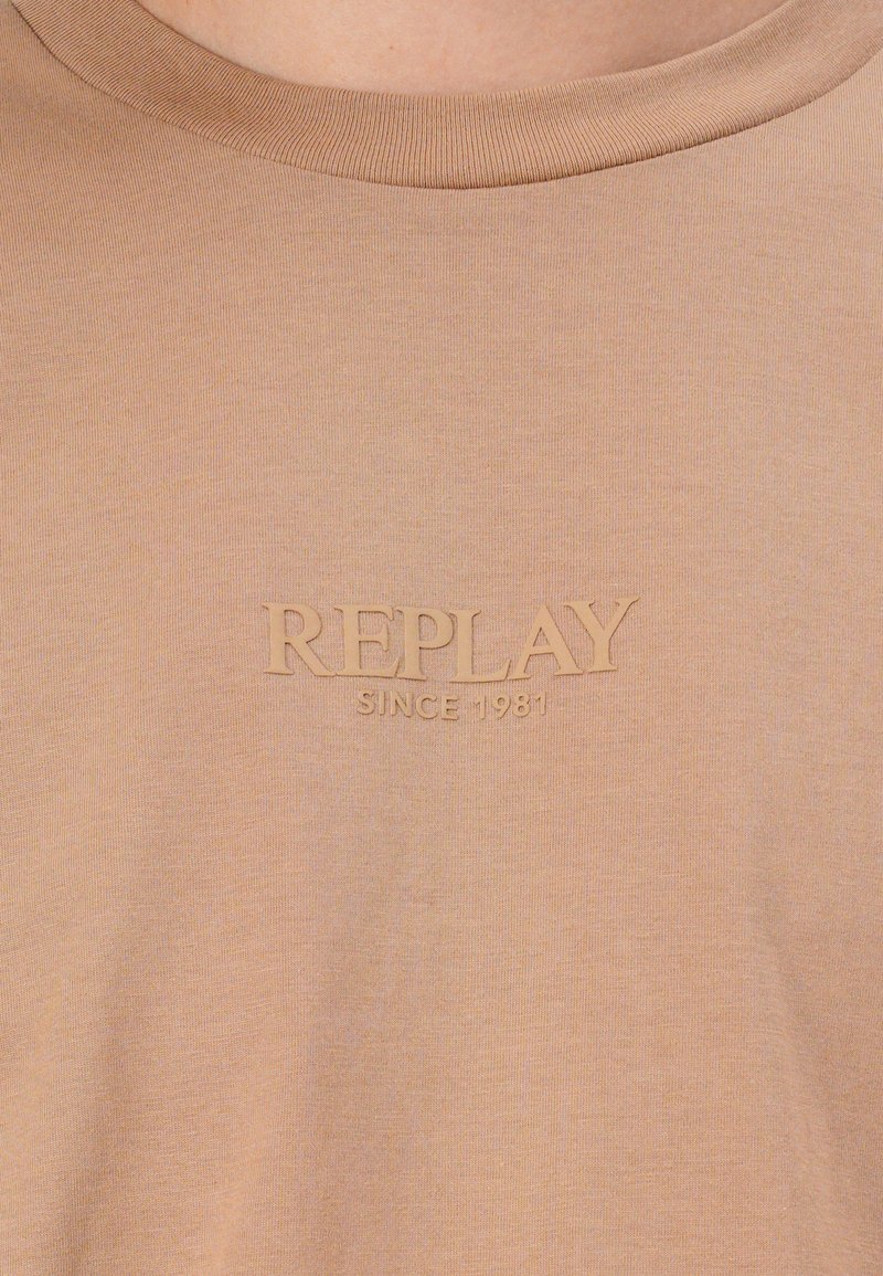 T-shirt in cotone beige con colletto a coste e logo in rilievo "REPLAY SINCE 1981" dello stesso colore. Texture morbida e liscia.
