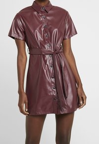 Bordeauxfarbenes Kunstlederhemdkleid mit Kragen, kurzen Ärmeln, durchgehender Knopfleiste, tailliertem Design und einer glatten, glänzenden Oberfläche.