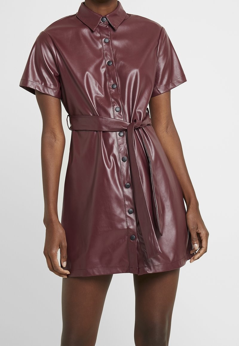 Bordeauxfarbenes Kunstlederhemdkleid mit Kragen, kurzen Ärmeln, durchgehender Knopfleiste, tailliertem Design und einer glatten, glänzenden Oberfläche.