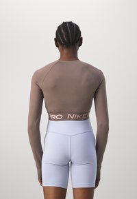 Person mit geflochtenem Haar, der ein langärmliges, kurzes Sportoberteil und hochgeschnittene helllilafarbene Shorts trägt, von hinten gesehen.