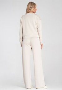 Jasnobeżowa, długorękawowa bluza o luźnym kroju i ściągaczami, zestawiona z dopasowanymi spodniami wide-leg. Miękka tkanina, minimalistyczny design.