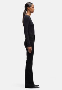 Czarna bluzka z długim rękawem i czarne rozkloszowane dżinsy noszone razem. Materiał wydaje się gładki, dopasowany krój, w połączeniu z butami na spiczastym nosku.