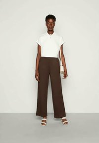 Top branco de mangas curtas, calças largas castanhas de cintura alta e sandálias brancas de tiras. Inclui uma pequena bolsa de ombro. Texturas suaves.