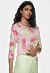 Lightweight, short-sleeve top with pink and green tropical print, featuring pineapples and leaves. Combined with light green pants.
