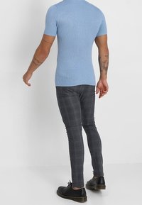 Světle modrý žebrovaný svetřík s krátkým rukávem zkombinovaný s slim-fit šedými kostkovanými kalhotami a černými botami, které ukazují přiléhavý, moderní siluetu.