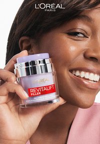 Crème-gel Revitalift Filler de L'Oréal dans un pot transparent avec un couvercle argenté et un dessus violet, tenue dans une main devant un fond clair.