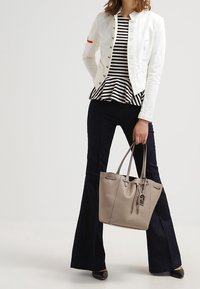 Duża beżowa skórzana torba tote o fakturowanym wykończeniu, z zapięciem na wiązanie i metką. Połączona z białą kurtką i pasek peplum w paski.