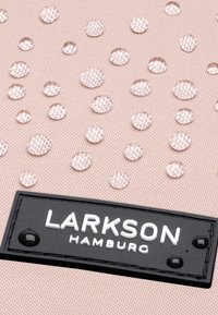 Világos rózsaszín anyag, átlátszó cseppekkel, fekete címkével, fehér szöveggel: "LARKSON HAMBURG." A textúrás felület fokozza a vizuális érdekességet.