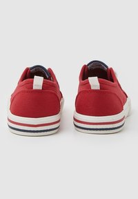 Rote Leinwand-Sneaker mit kontrastierender weißer Sohle, strukturiertem Obermaterial und rot-weiß-blauen Streifendetails am Rand der Sohle.