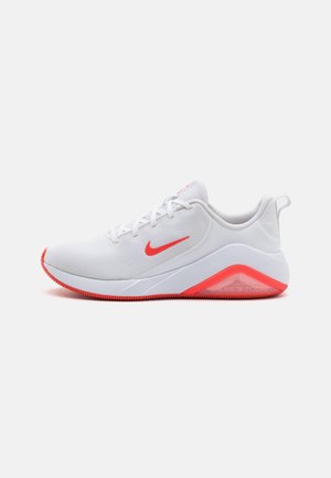 Baskets de sport blanches avec le swoosh rouge de Nike et des accents sur la semelle, tige en mesh, fermeture à lacets et amorti visible au talon.