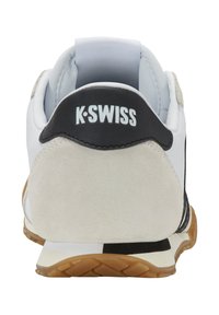 Basket K-Swiss avec une tige en cuir blanc, un talon en suede gris, des accents noirs et une semelle en caoutchouc gum avec un motif en chevrons.