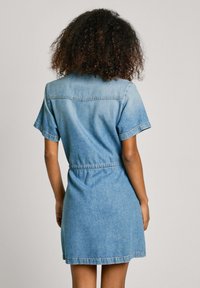 Denim kleita gaiši zilā krāsā, īsām piedurknēm, ar sašaurinātu jostas vietu, apkakli un taisnu apakšdaļu. Iekļauj viegli izsmēķētu faktūru un apakšējo josto.