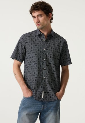 Kurzarm-Hemd mit Knopfleiste in Marineblau, mit weißen Wellendesigns, Kragen und geradem Saum. Hergestellt aus leichtem, strukturiertem Stoff.