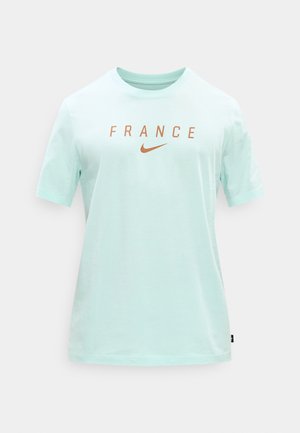Lichtblauw T-shirt met korte mouwen, met de tekst "FRANCE" en een oranje Nike Swoosh-logo centraal op de borst, tegen een effen achtergrond.
