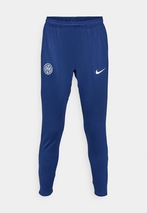 Navy blue athletic pants made of smooth fabric. Features a white Nike logo and a round team emblem on the left thigh. Elastic waistband.