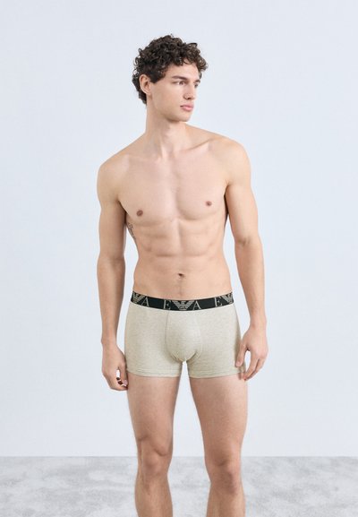 Beige bomuldsboxershorts med sort elastik i taljen med logo. Glat tekstur, tætsiddende design og midt på låret i længden.