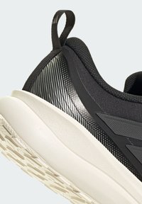 Black athletic shoe with textured white sole, pull tab at heel, and patterned synthetic overlay on upper side.