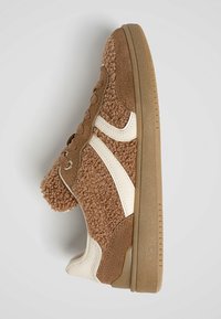 Baskets marron texturées avec des accents blancs, semelle beige et fermeture à lacets, vues de profil sur un fond uni.