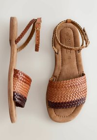Sandali intrecciati marroni con suola piatta; presentano cinturini in pelle intrecciata e una fibbia. La parte superiore ha una texture bicolore che passa da un marrone chiaro a un marrone scuro.