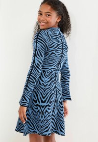 Blau-schwarz gestreiftes Strickkleid mit langen Ärmeln, passgenauer Oberteil und ausgestelltem Rock, der ein strukturiertes Design und ein kontrastierendes Muster zeigt.