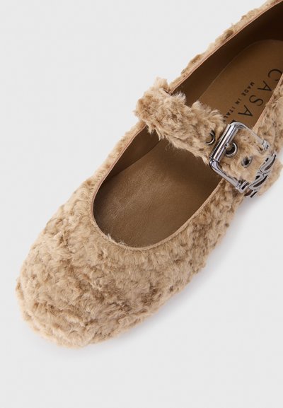 Beige furry flat shoe with a round toe, featuring a silver buckle strap. Soft textured surface and a smooth inner lining.