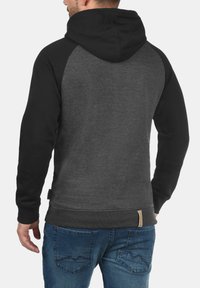 Capuchon sweatshirt met zwarte mouwen en een donkergrijs lichaam. Bevat een gestructureerde afwerking en een geweven label aan de zoom. Draagt met een blauwe jeans.