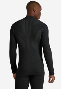 Długi rękaw sportowej koszulki w ciemnoszarym kolorze z teksturowanym wzorem, dopasowanym krojem i otworami na kciuki przy mankietach. Widok z tyłu podkreśla detale przeszyć.