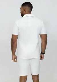 Chemise blanche à manches courtes et shorts assortis avec un motif texturé. Design à coupe droite, col classique, avec des accents subtils.