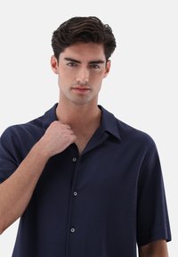 Marineblaues Kurzarmhemd mit strukturiertem Muster, geknöpftem Kragen und zwei sichtbaren Knöpfen. Glattes Material und lockere Passform.