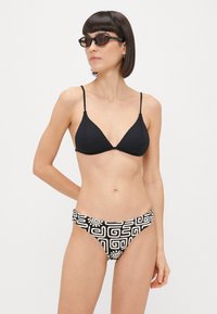 Μαύρο ριμπ μπικίνι τοπ με ρυθμιζόμενες τιράντες, σε συνδυασμό με μαύρα και λευκά μπικίνι σόρτς με γεωμετρικά σχέδια.