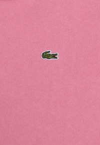 Pink cotton shirt featuring a green embroidered crocodile logo. The fabric has a smooth texture with a fitted design.