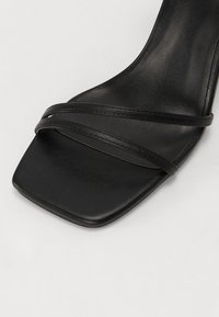 Sandal con tacco alto nero caratterizzata da punta quadrata, cinturini sottili e una superficie in pelle liscia con una texture opaca.