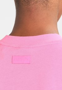 Rosa bomullströja med krage och en rektangulär etikett som läser "FENTY," med en liten logotyp. Slät textur, enkel design och inga synliga mönster.