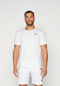 Biała sportowa koszulka z krótkim rękawem wykonana z lekkiego materiału, z małym czarnym logo Puma na lewej piersi. W połączeniu z białymi szortami.