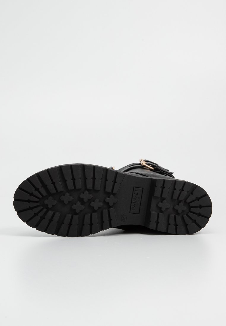 Semelle de botte en caoutchouc noir avec un motif de semelle profond, arborant un logo rectangulaire. Forme structurée avec une texture pour une meilleure adhérence et stabilité.