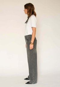 Jean gris à jambes larges, taille haute, avec des coutures contrastantes. Associé à un t-shirt blanc et des chaussures noires à bouts pointus, agrémenté d'une écharpe à motifs.