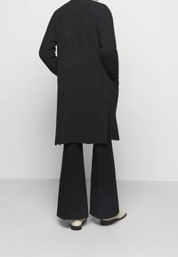 Dlouhý, tmavě šedý pletený kardigan s volným střihem, bočními rozparky a ribbovým povrchem, doplněný o kalhoty se širokými nohavicemi a krémové boty.