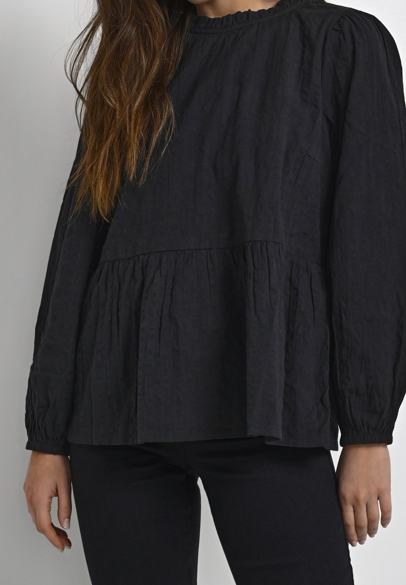 Haut noir à manches longues avec un col froncé et un design à volants, fabriqué en tissu texturé, avec des manches bouffantes et des poignets élastiques.